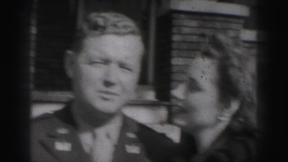 The man in uniform and a woman stand close together outside a brick house in the 1975 Harrisburg home-movie clip.