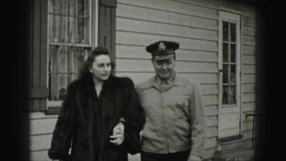 A closer Harrisburg frame shows the woman in a dark coat and the uniformed man walking toward camera beside shuttered windows.