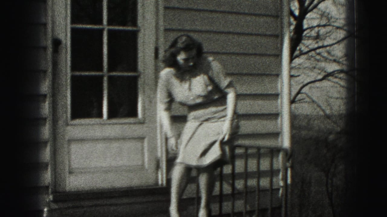 Woman sits sideways on a porch railing outside a house.
