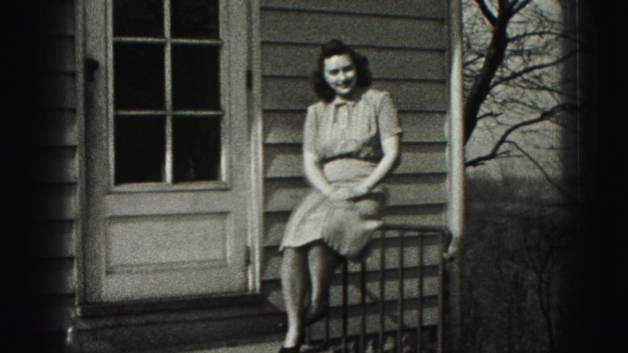 In Harrisburg, Pennsylvania, a woman sits on a porch railing in a light dress, smiling toward the camera in 1975 home-movie footage.