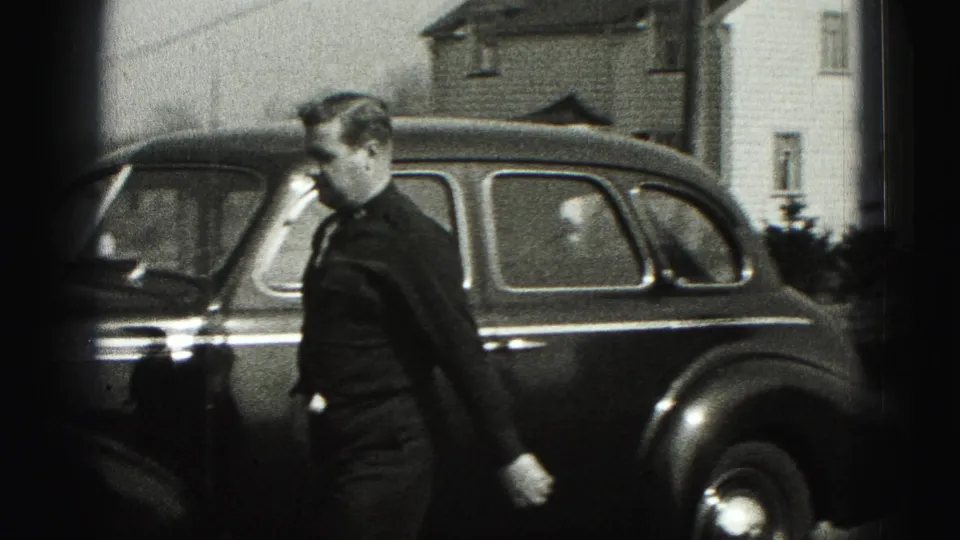 The man moves along the side of the dark sedan, partly blurred by motion, in the 1975 Harrisburg home-movie clip.
