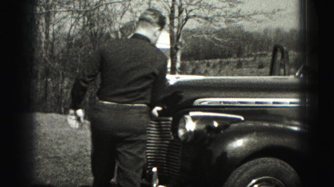 In Harrisburg, Pennsylvania home-movie footage from 1975, a man stands by the front fender of an older car near bare trees.