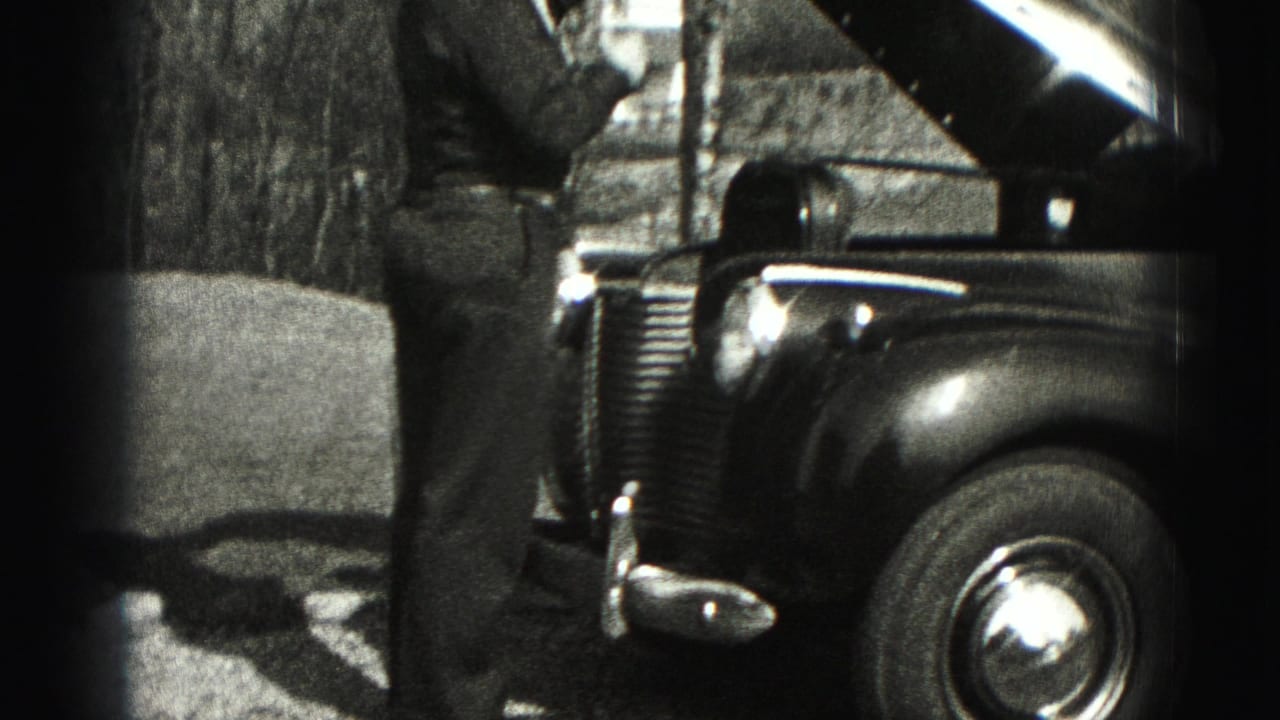 A man stands at the front of an older car with the hood lifted, filmed outdoors in 1975 Harrisburg-area home-movie footage.