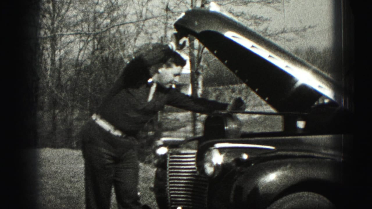 In Harrisburg, Pennsylvania footage from 1975, a man in a suit leans over the raised hood of a classic car outdoors.