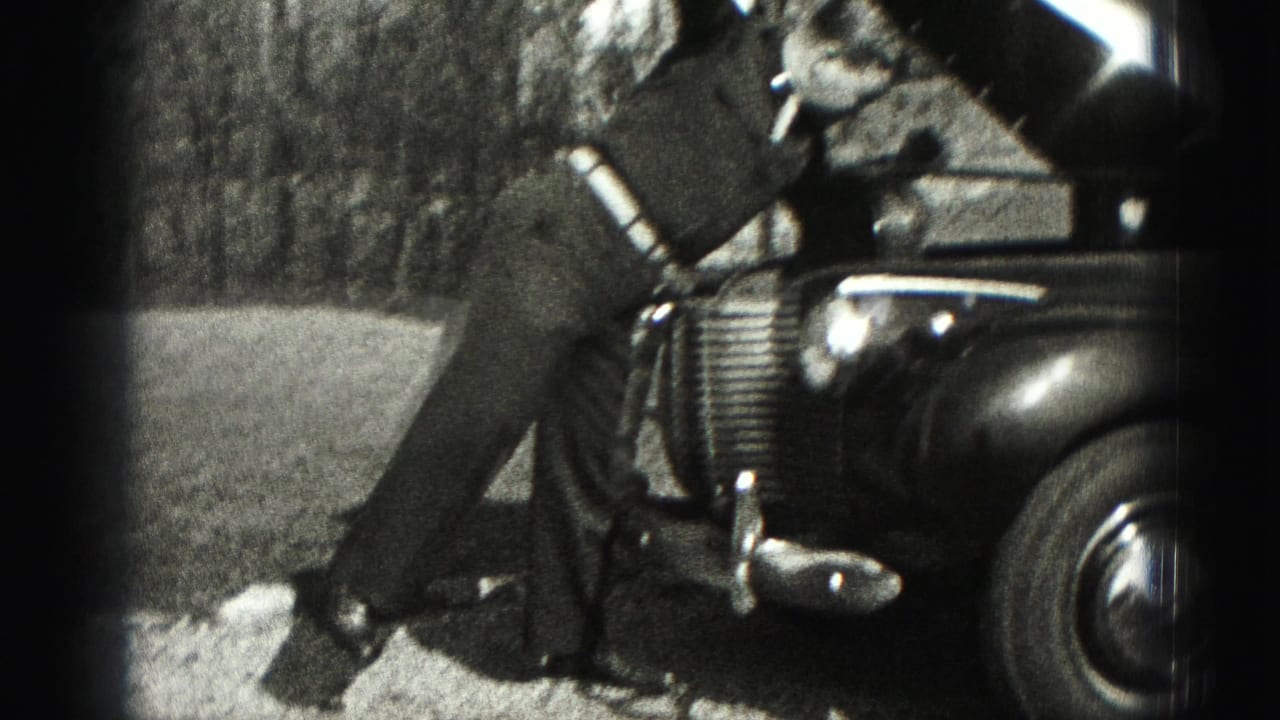 A suited man stands near the open hood and front fender of an older car in the 1975 Harrisburg home-movie footage.