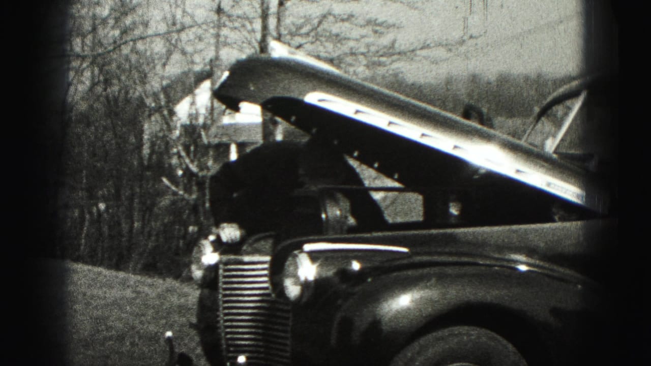 The open hood and front end of a vintage car appear in a Harrisburg-area outdoor setting with bare trees behind it.