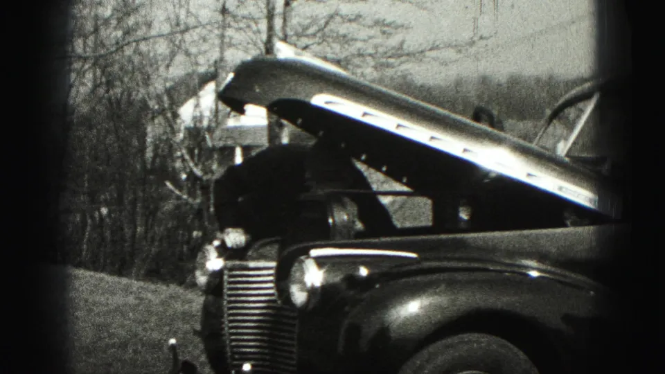 The open hood and front end of a vintage car appear in a Harrisburg-area outdoor setting with bare trees behind it.
