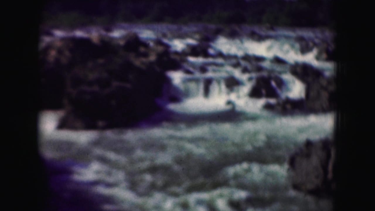 1975 8mm frame of blue-green river rapids moving through rocky terrain, with soft focus and dark frame edges.