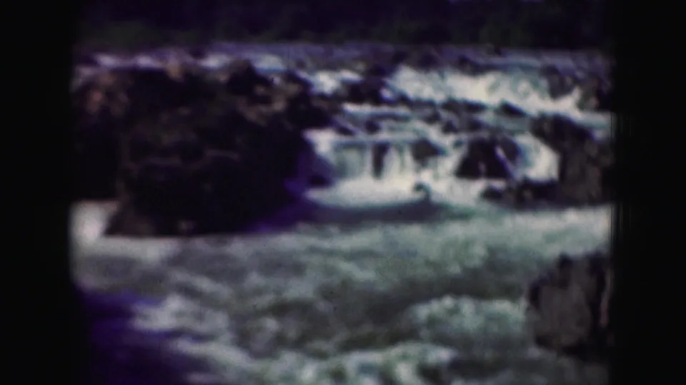 1975 8mm frame of blue-green river rapids moving through rocky terrain, with soft focus and dark frame edges.