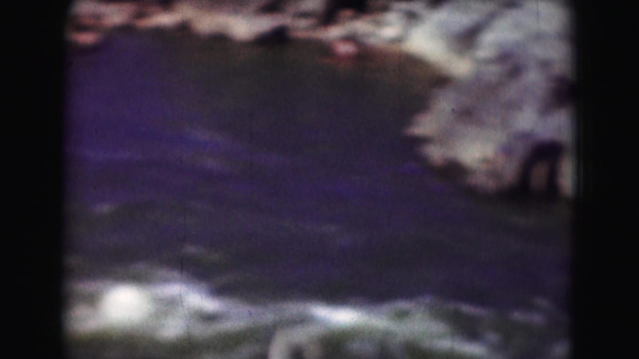 Soft, dark view of rushing water and rocks with heavy shadow around the frame.