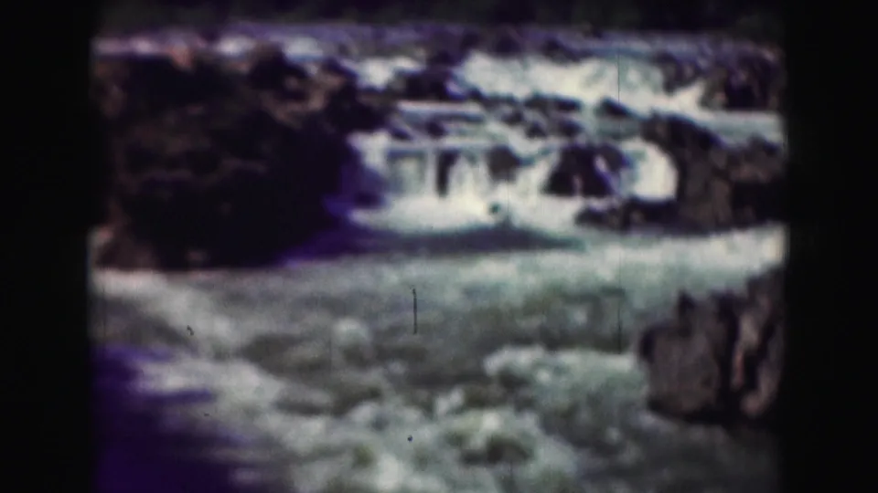 1975 8mm home-movie frame of rushing water and rocks in the Washington, DC area, with soft focus and dark film borders.
