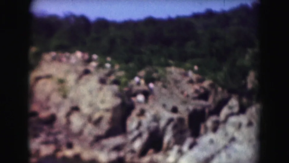 1975 8mm Washington DC footage showing a rocky river overlook with distant visitors, tree cover, and blue sky.