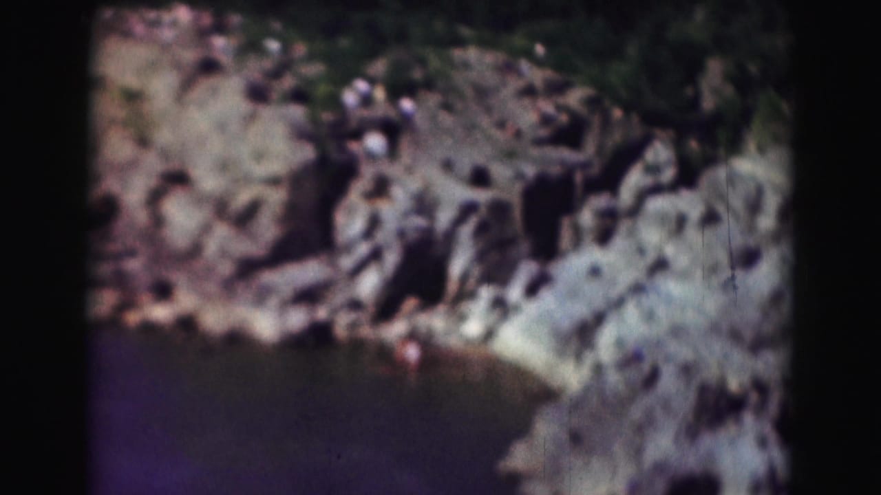 1975 8mm Washington DC view of rock ledges above a calm pool, with small distant visitors near the overlook.