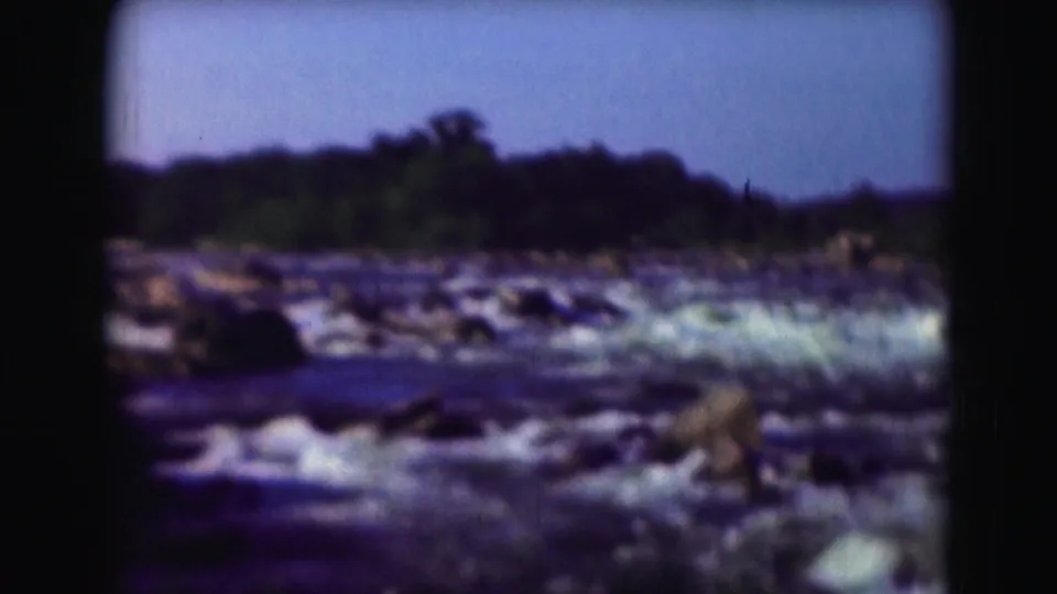1975 8mm Washington DC footage showing low river rapids flowing over rocks below a tree-lined horizon.