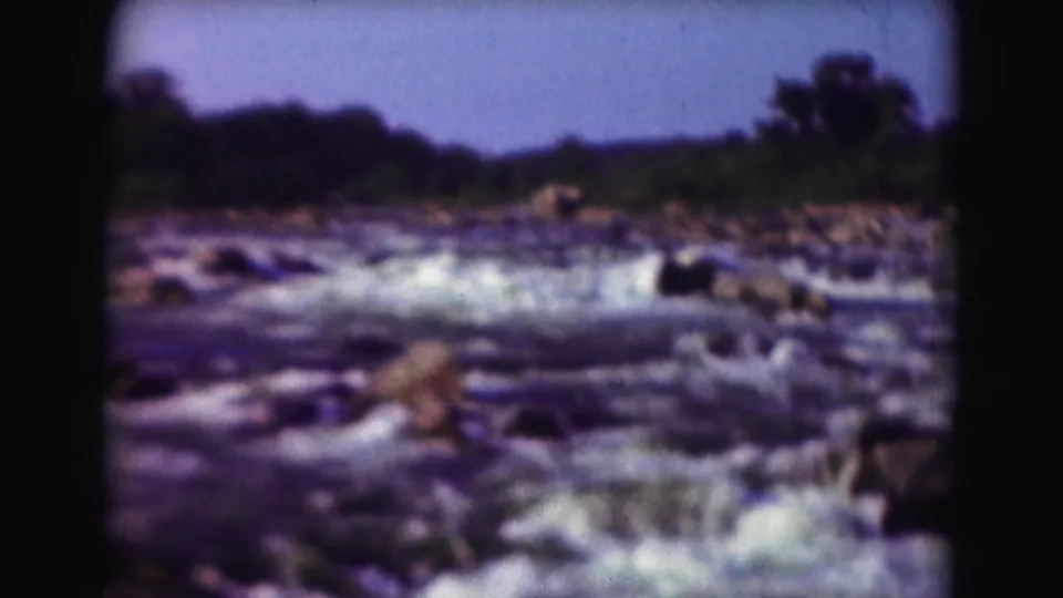 1975 8mm Washington DC wide view of river rapids, scattered rocks, and trees along the far bank.
