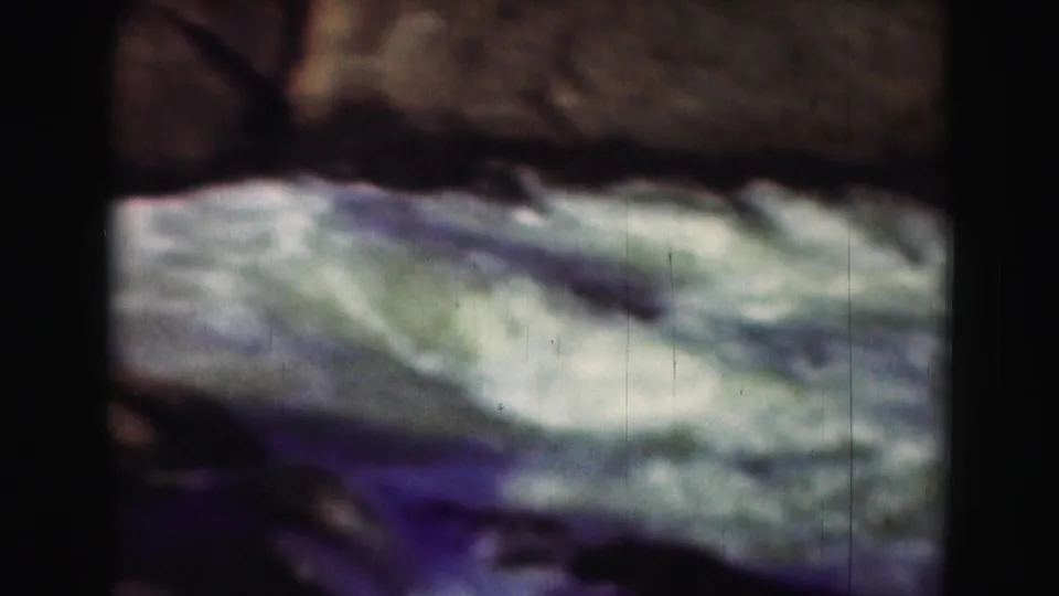 1975 8mm Washington, DC-area footage showing blurred white water rapids framed by dark rocks and heavy film borders.