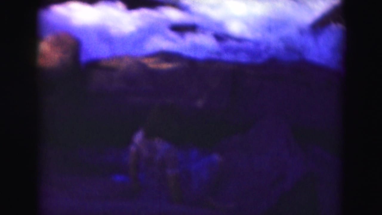 Soft 8mm frame of a girl low on rocks near dark rushing water.