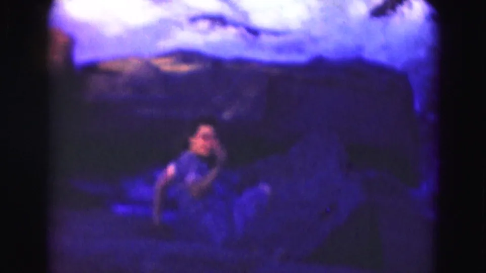 Blue-purple 1975 8mm frame near Washington, DC with a teenage girl on rocks looking back from beside the river.
