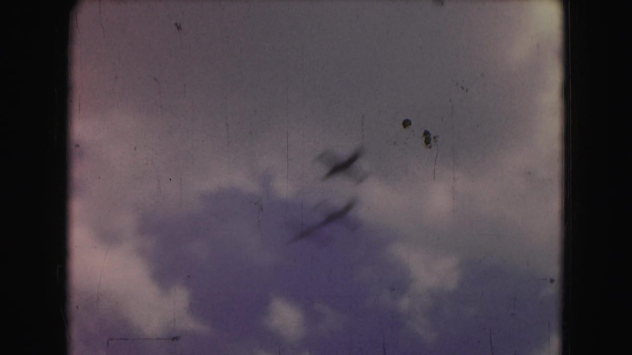 Three small dark jets pass across a cloudy sky on faded 8mm film.