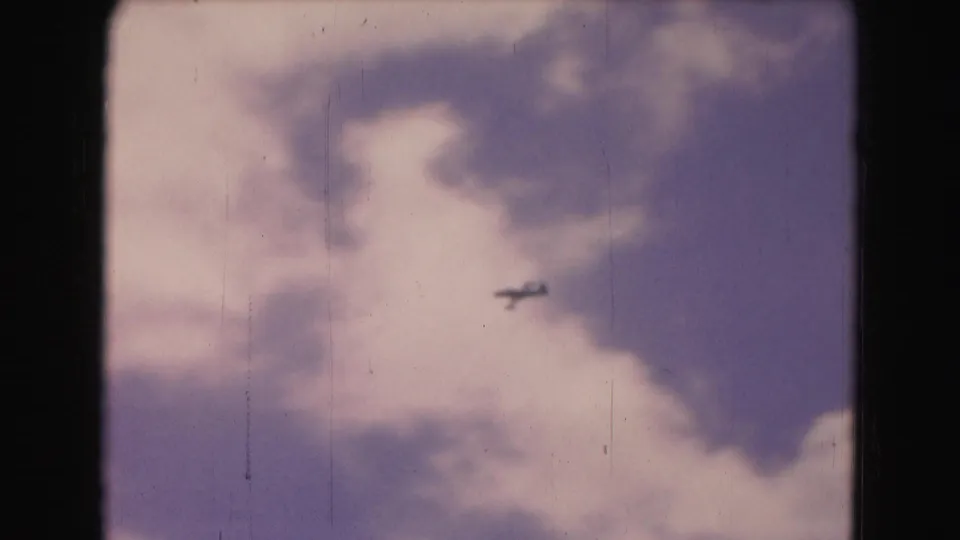 1975 8mm home-movie frame of a small plane crossing a cloudy sky in the Washington DC travel footage.
