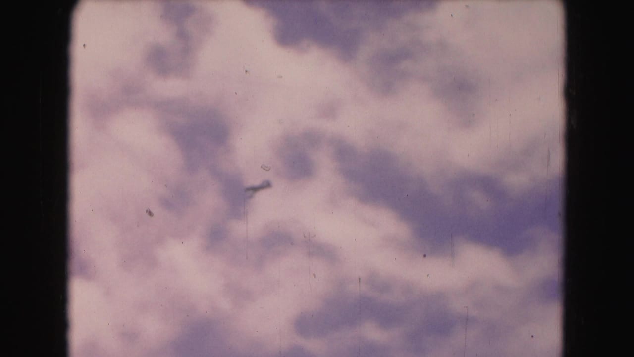 A distant aircraft appears in the cloudy sky, with dark 8mm frame edges and faded color visible.