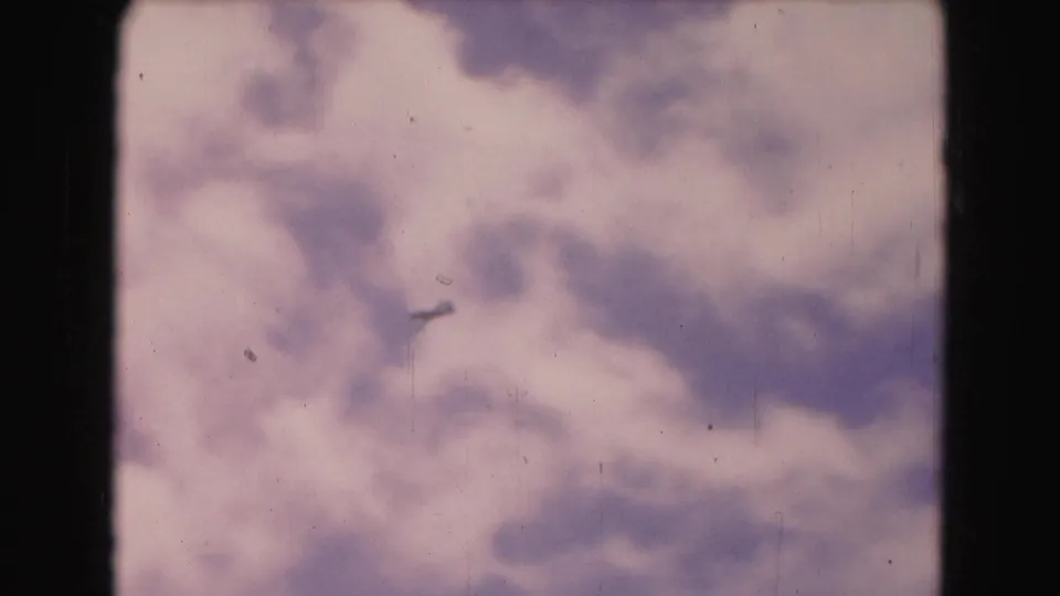 A distant aircraft appears in the cloudy sky, with dark 8mm frame edges and faded color visible.
