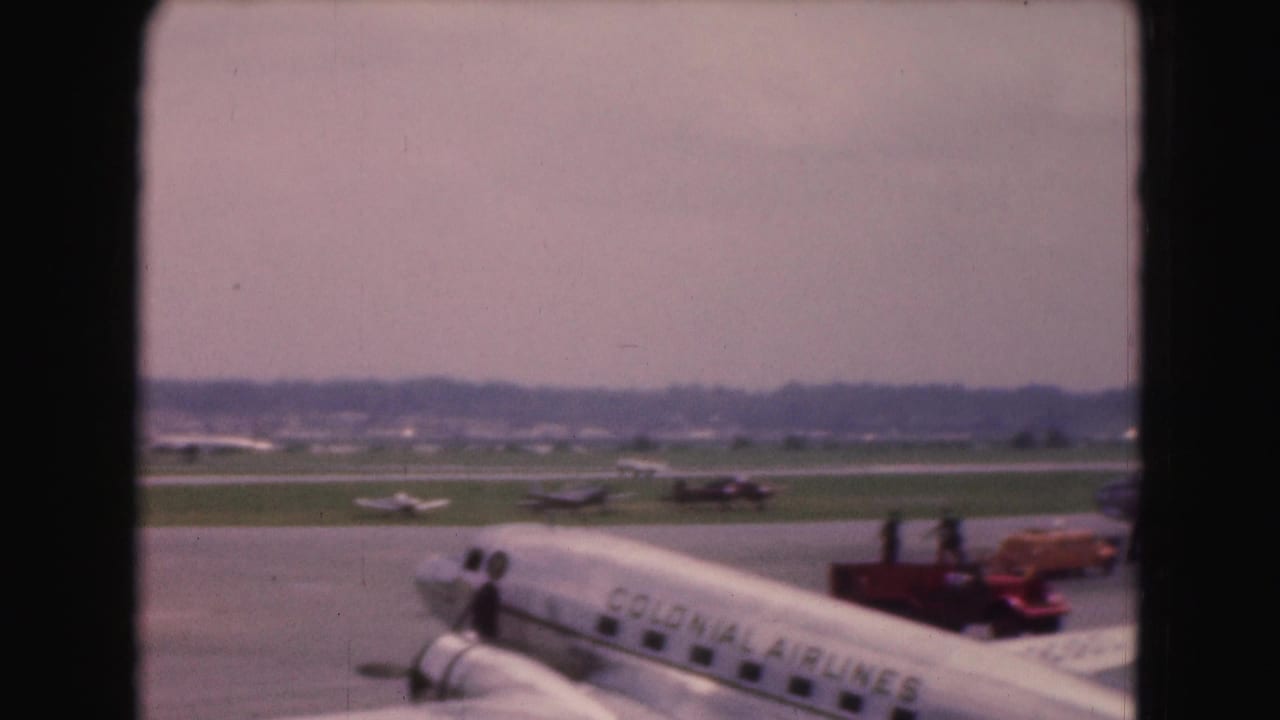 Parked airliner on the tarmac with airline lettering, service vehicles, and distant planes beyond the runway.