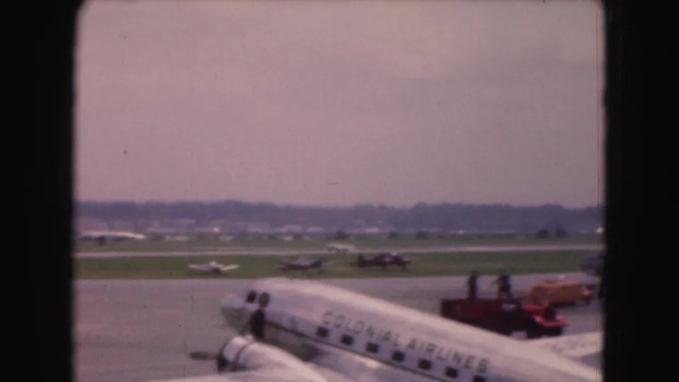 1975 Washington DC tarmac scene with a parked airliner, visible airline lettering, ground vehicles, and aircraft in the distance.