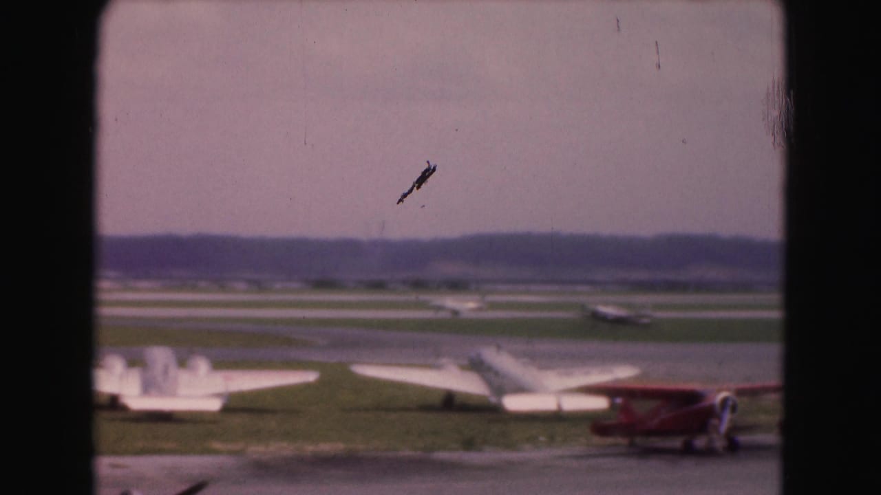 Runway view with several light aircraft, a red biplane, and a small plane shape high in the sky.