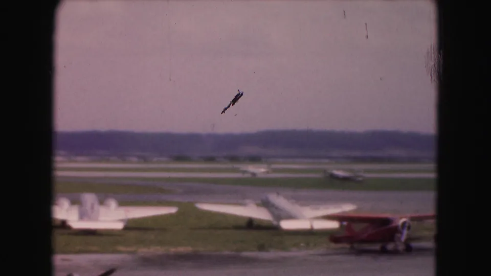 Washington, DC-area 8mm airfield footage shows parked planes, a red biplane, runways, and a small aircraft or mark visible in the sky.