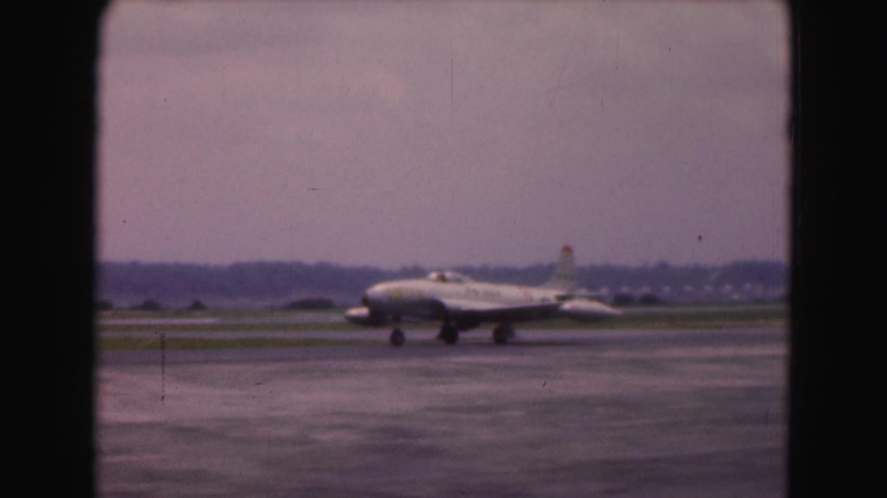White passenger jet taxiing on a wet runway with dark film borders.