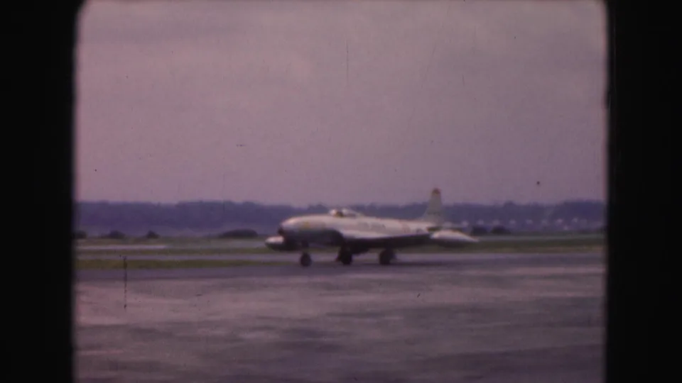 A white commercial airliner taxis across a wet Washington, DC airport runway in 1975 home-movie footage.