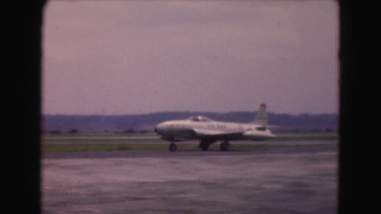 The airliner continues taxiing across the wet tarmac, seen at a distance in 1975 Washington, DC airport footage.