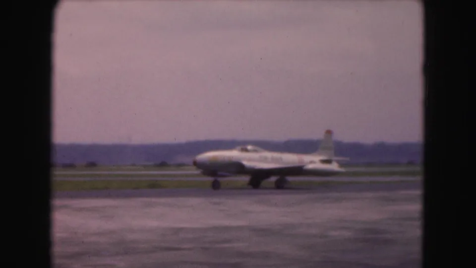 The airliner continues taxiing across the wet tarmac, seen at a distance in 1975 Washington, DC airport footage.