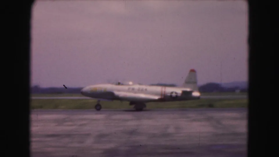 1975 Washington DC 8mm frame showing a white jet with U.S. star insignia taxiing across an airfield runway.