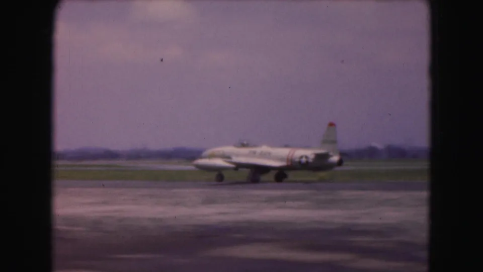 Soft 8mm frame of a white military-marked jet taxiing at a Washington DC area airfield in 1975.