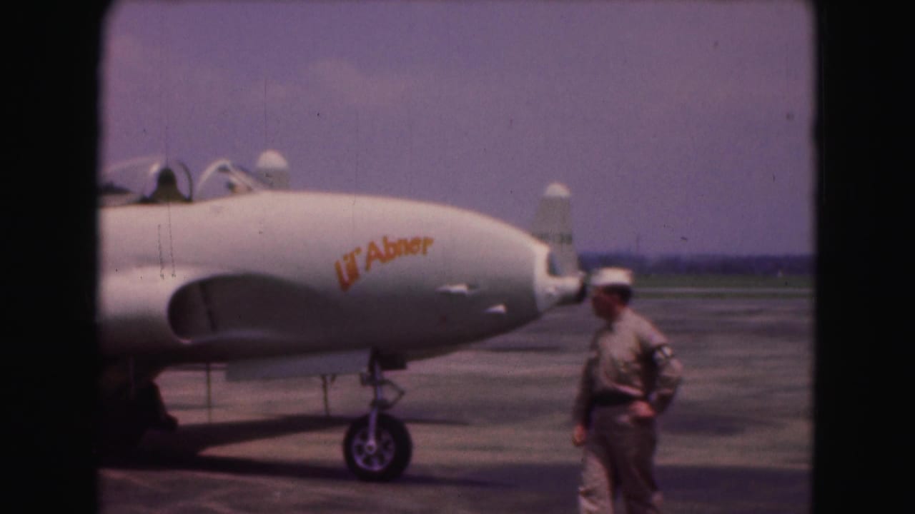 Close 1975 Washington, DC 8mm view of a military jet nose marked Lil' Abner with a uniformed man standing beside it.