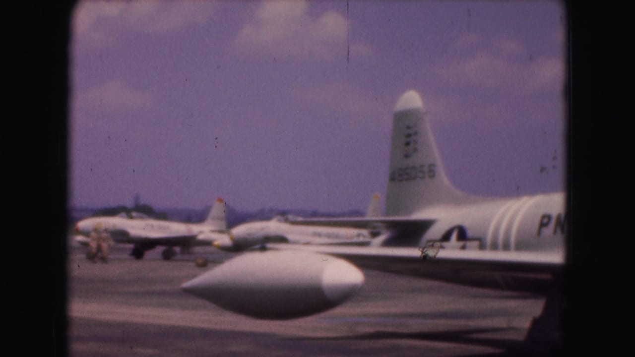 1975 8mm airfield view in Washington DC showing a white jet foreground and several parked military aircraft behind it.