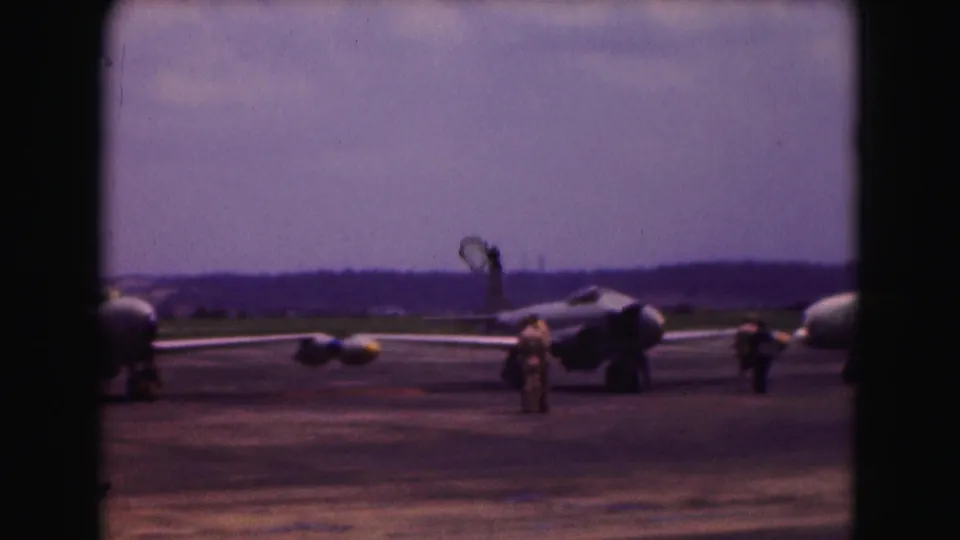 1975 Washington DC 8mm frame showing jet aircraft on an airport tarmac with ground crew under a hazy sky.