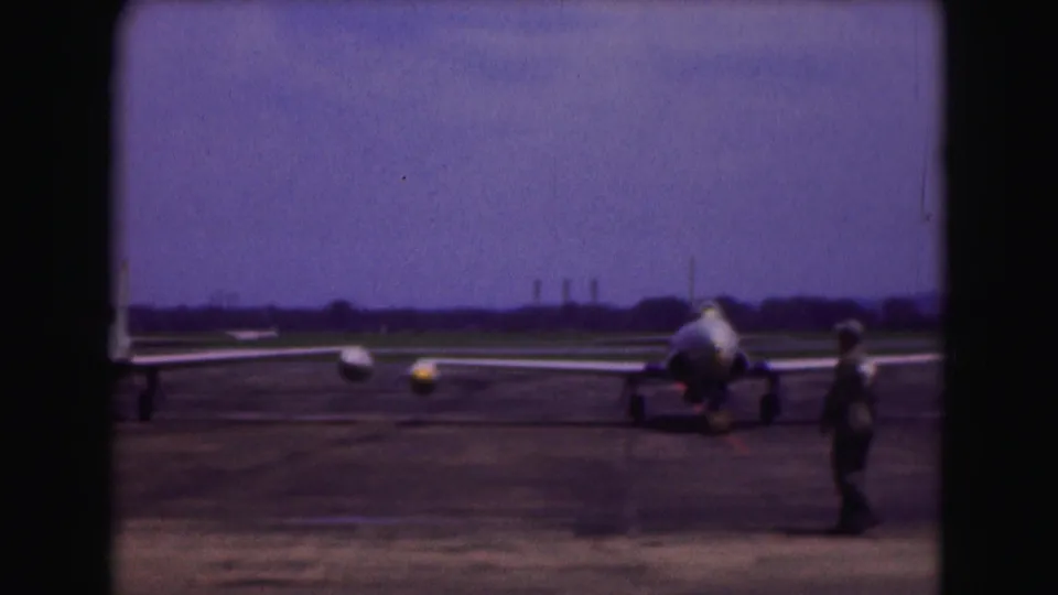 Wide 1975 Washington DC tarmac view with a parked jet aircraft, distant runway, and a walking figure at right.