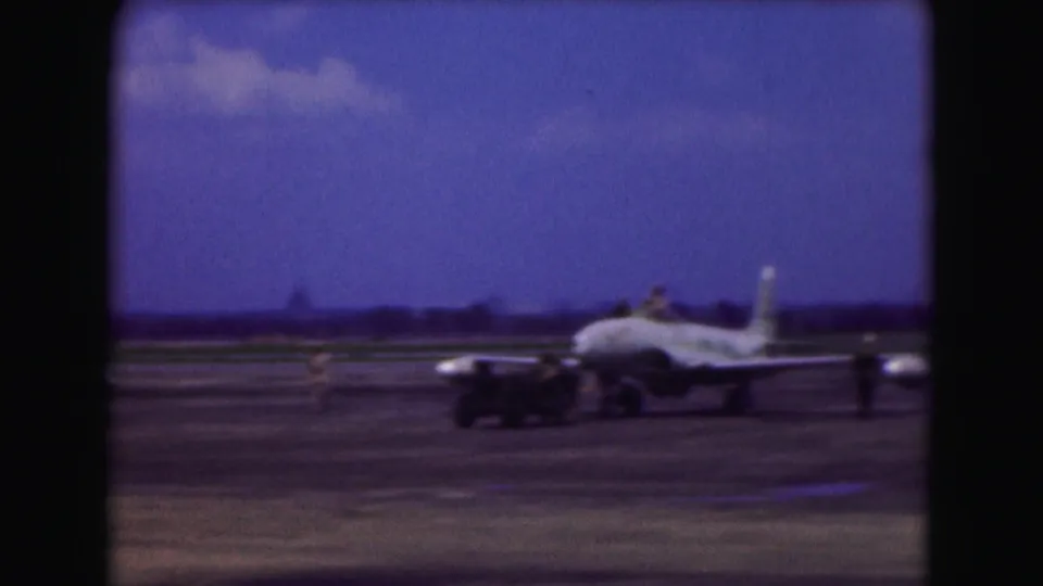 Side view of a military jet on a runway, with nearby equipment and soft 8mm motion blur.