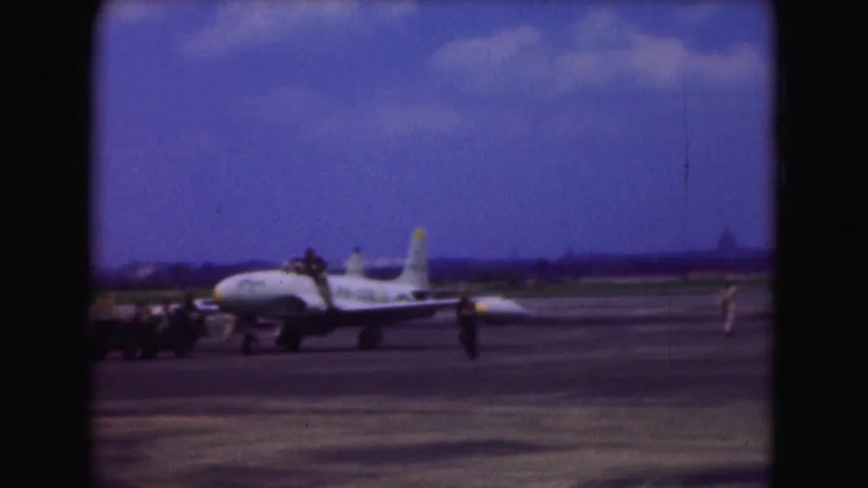 Military jet on a Washington, DC runway in 1975, with several ground personnel and equipment visible nearby.