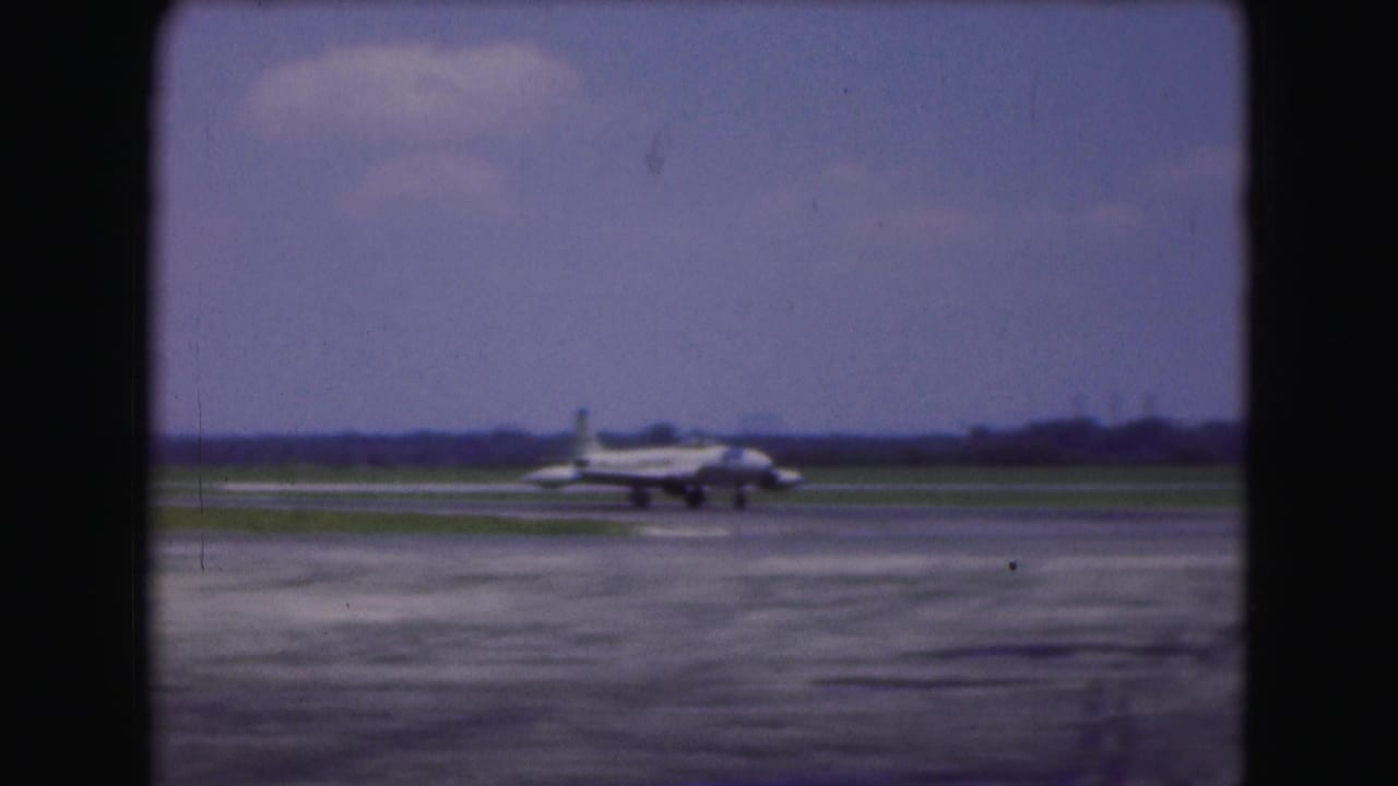 1975 Washington DC airport home-movie frame showing a commercial jet taxiing across the tarmac beyond a dark window-like edge.