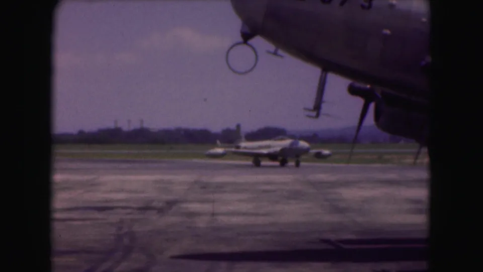 The closing frame keeps the distant jet on the runway while a nearby aircraft nose and landing gear edge dominate the upper right foreground.