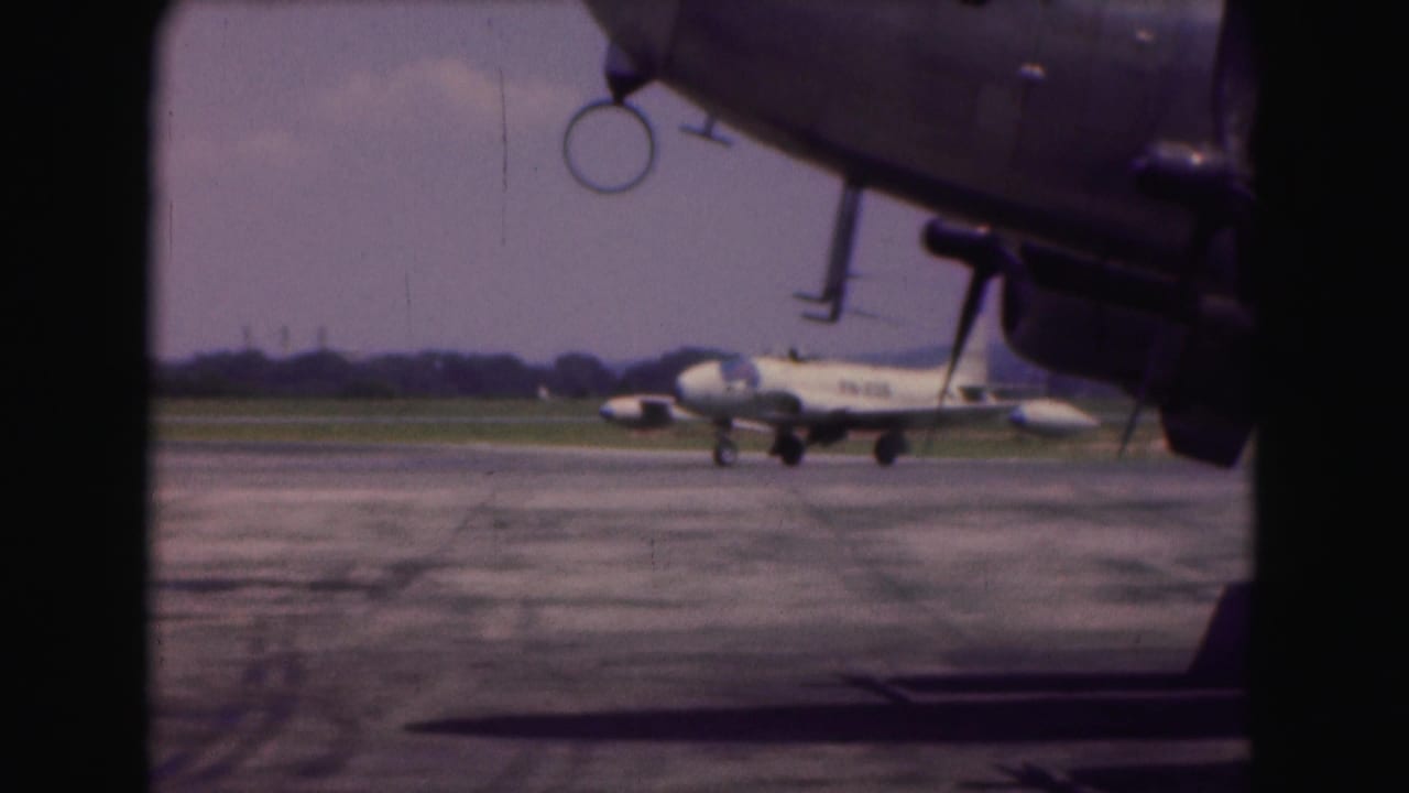 White military jet taxiing on a runway with another aircraft nose in the foreground.