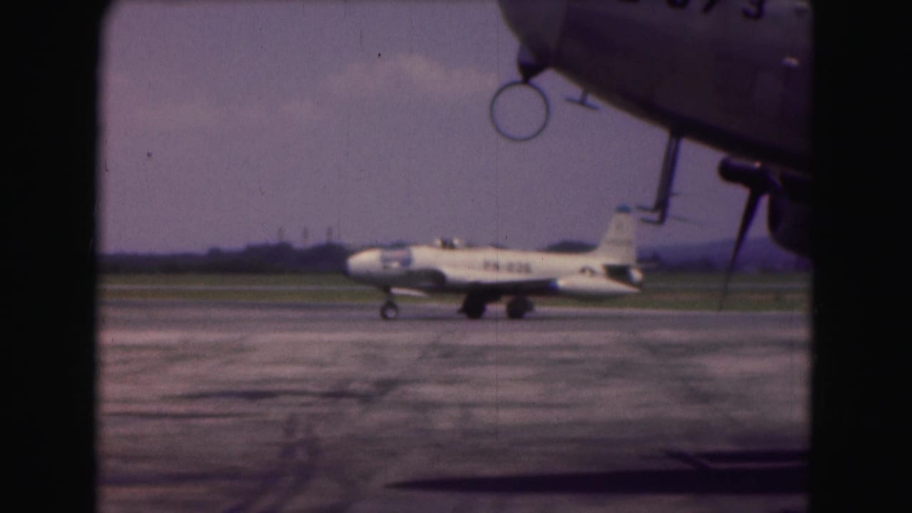 1975 Washington, DC 8mm frame of a white military jet taxiing on a broad airfield surface with markings visible on the fuselage.