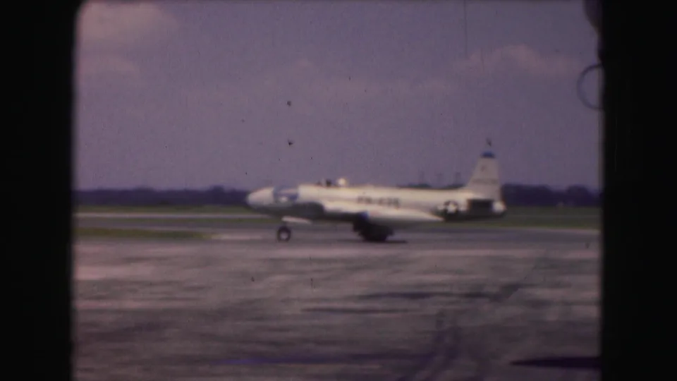 Side view from 1975 Washington, DC footage showing a white military jet taxiing across tarmac with a U.S. star insignia visible.