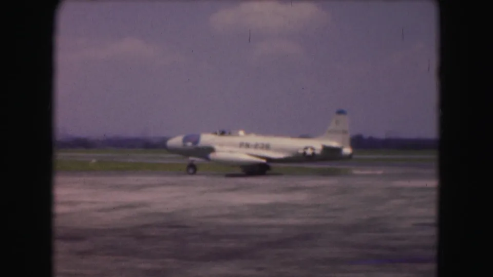 Final 1975 Washington, DC frame showing the white military jet moving along the runway, with soft grain and faded color from the 8mm scan.