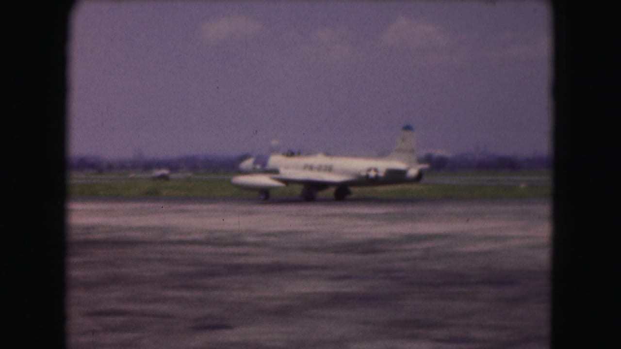 1975 Washington DC 8mm frame with a white military-marked aircraft continuing along the runway, partly soft from film focus.