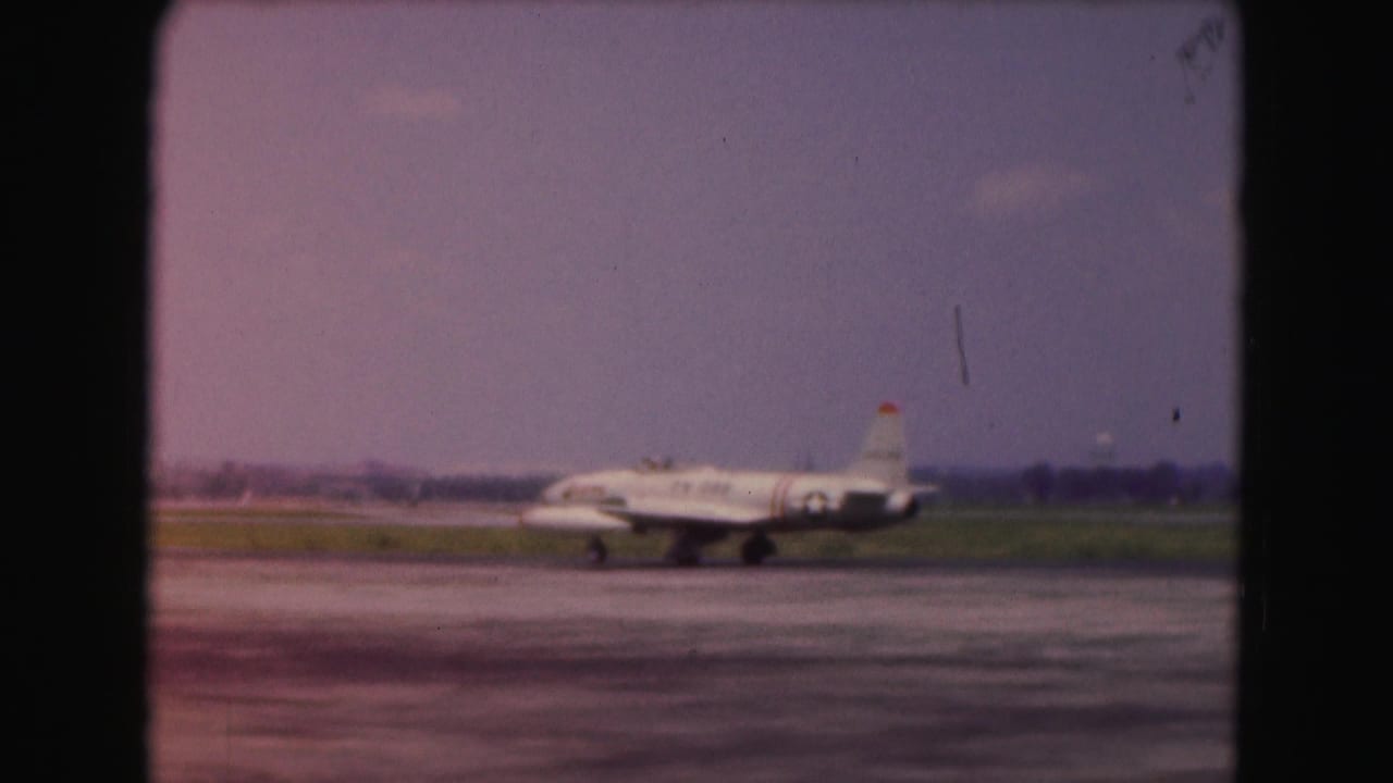 Small jet aircraft on a runway seen through a soft 8mm film frame.